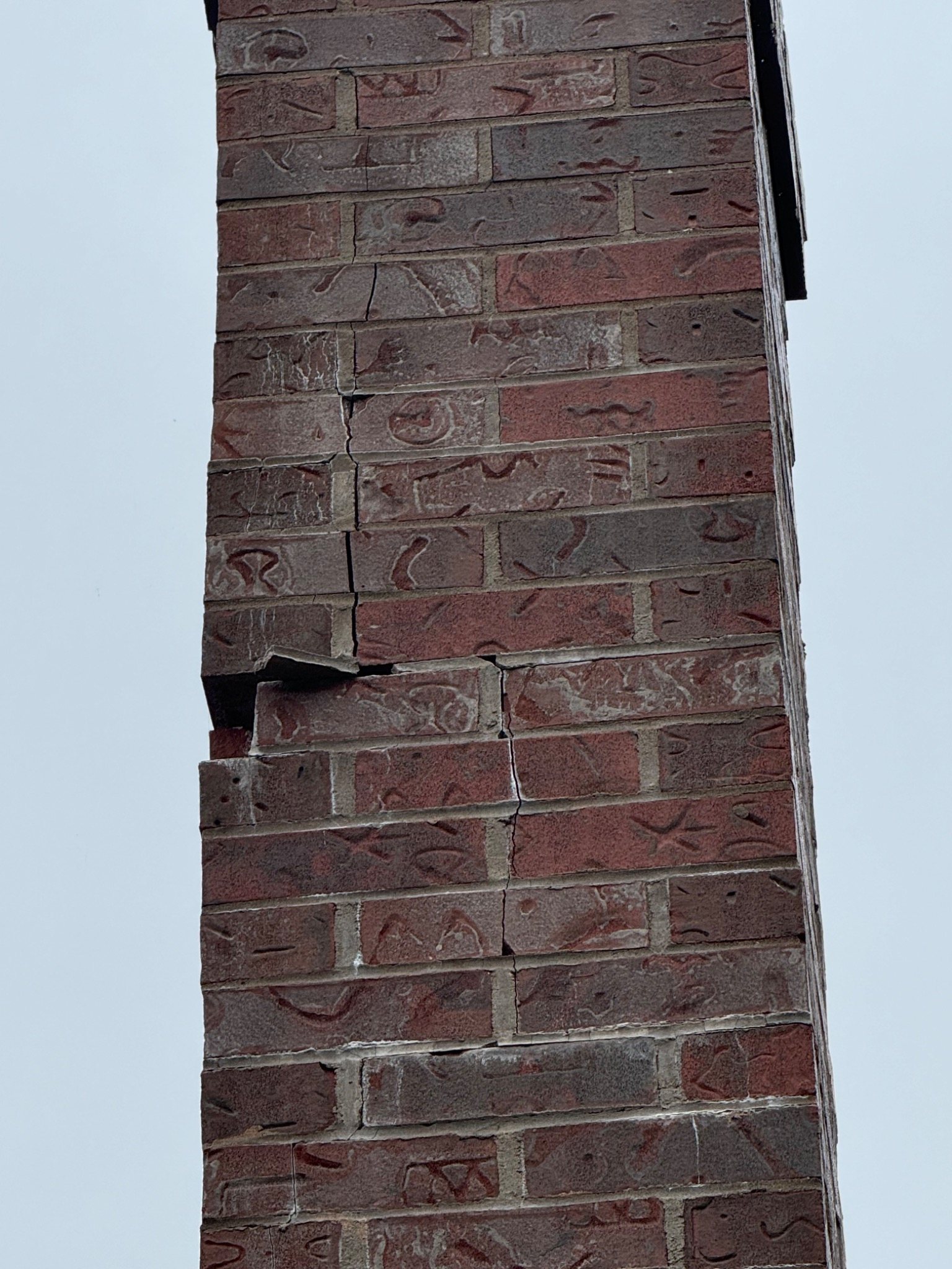 Tall brick chimney with vertical cracking and displaced masonry courses
