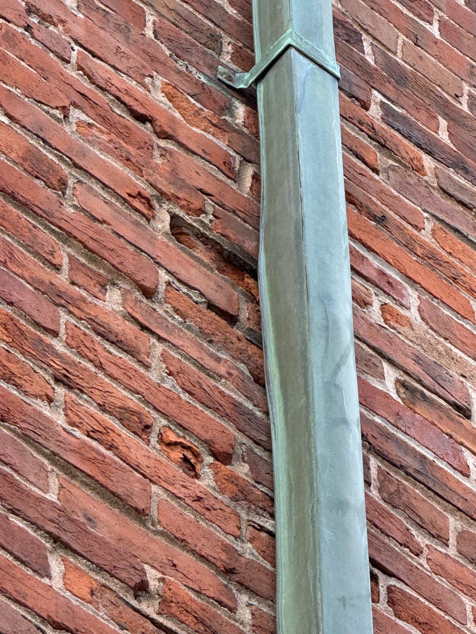 Weathered brick masonry near a downspout showing deterioration associated with repeated water exposure