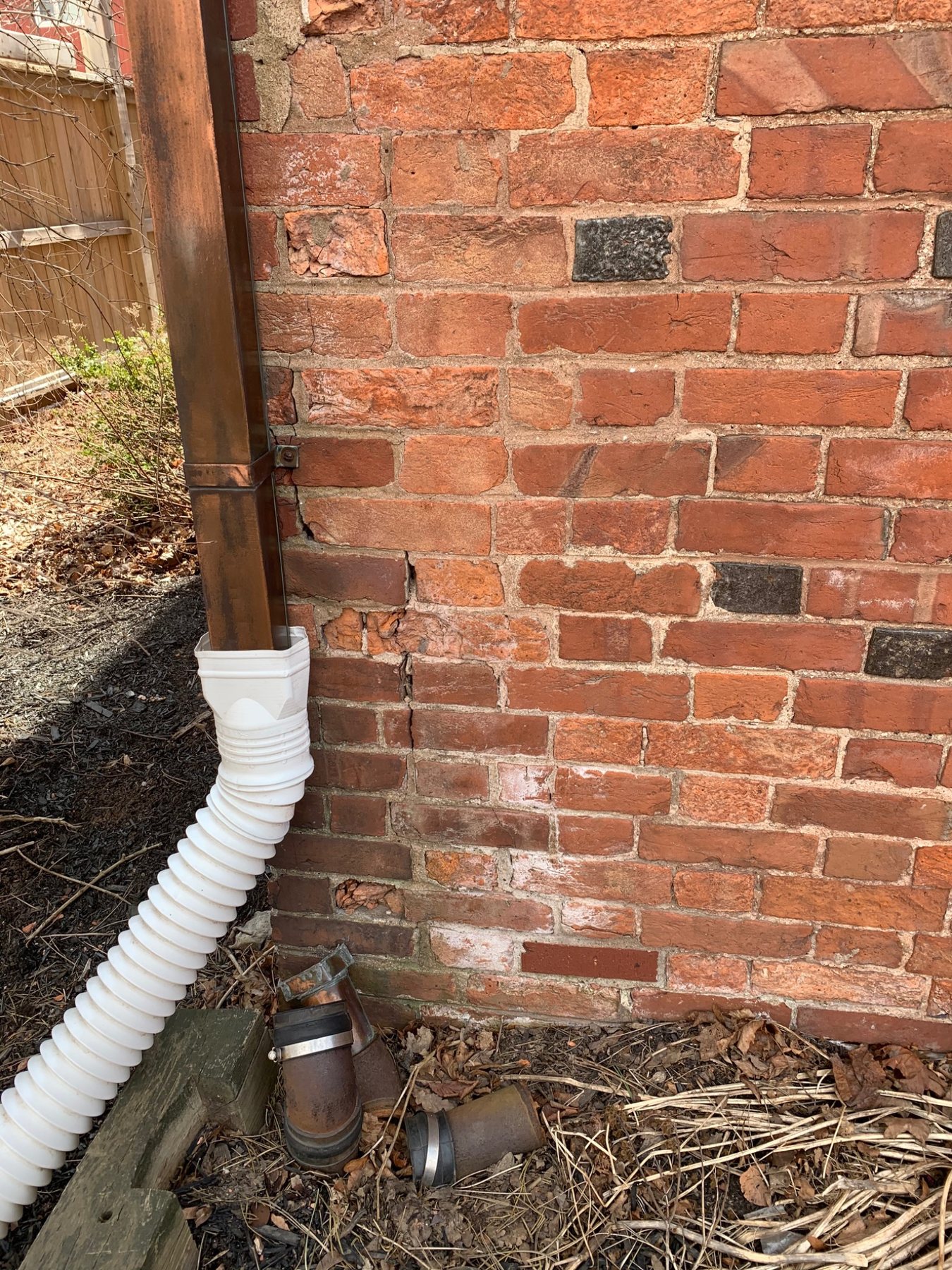 Downspout discharge beside deteriorated brick masonry near grade in PEI