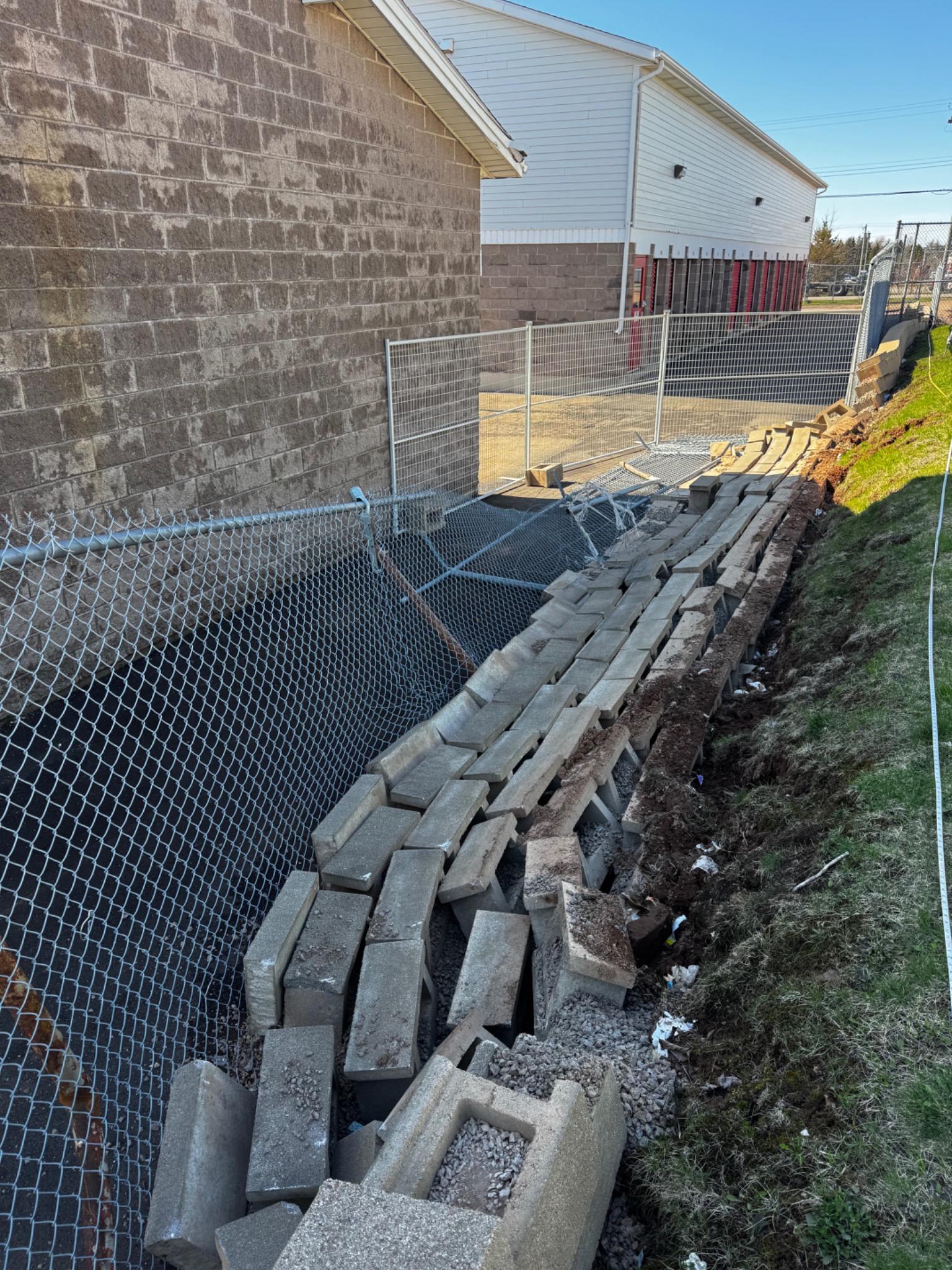 Retaining wall blocks collapsed along a sloped site, showing major wall failure and displaced units