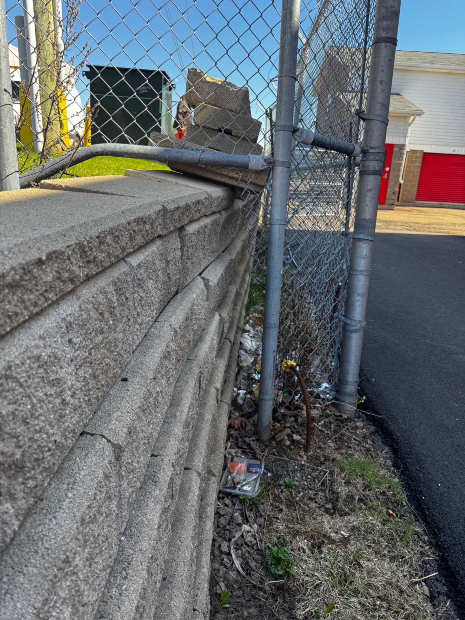 Retaining wall face leaning outward beside a chain-link fence, showing horizontal movement and misalignment