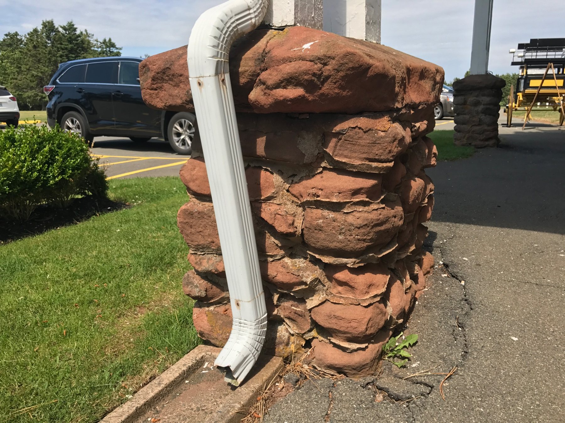 Downspout terminating beside red sandstone masonry at grade in Prince Edward Island