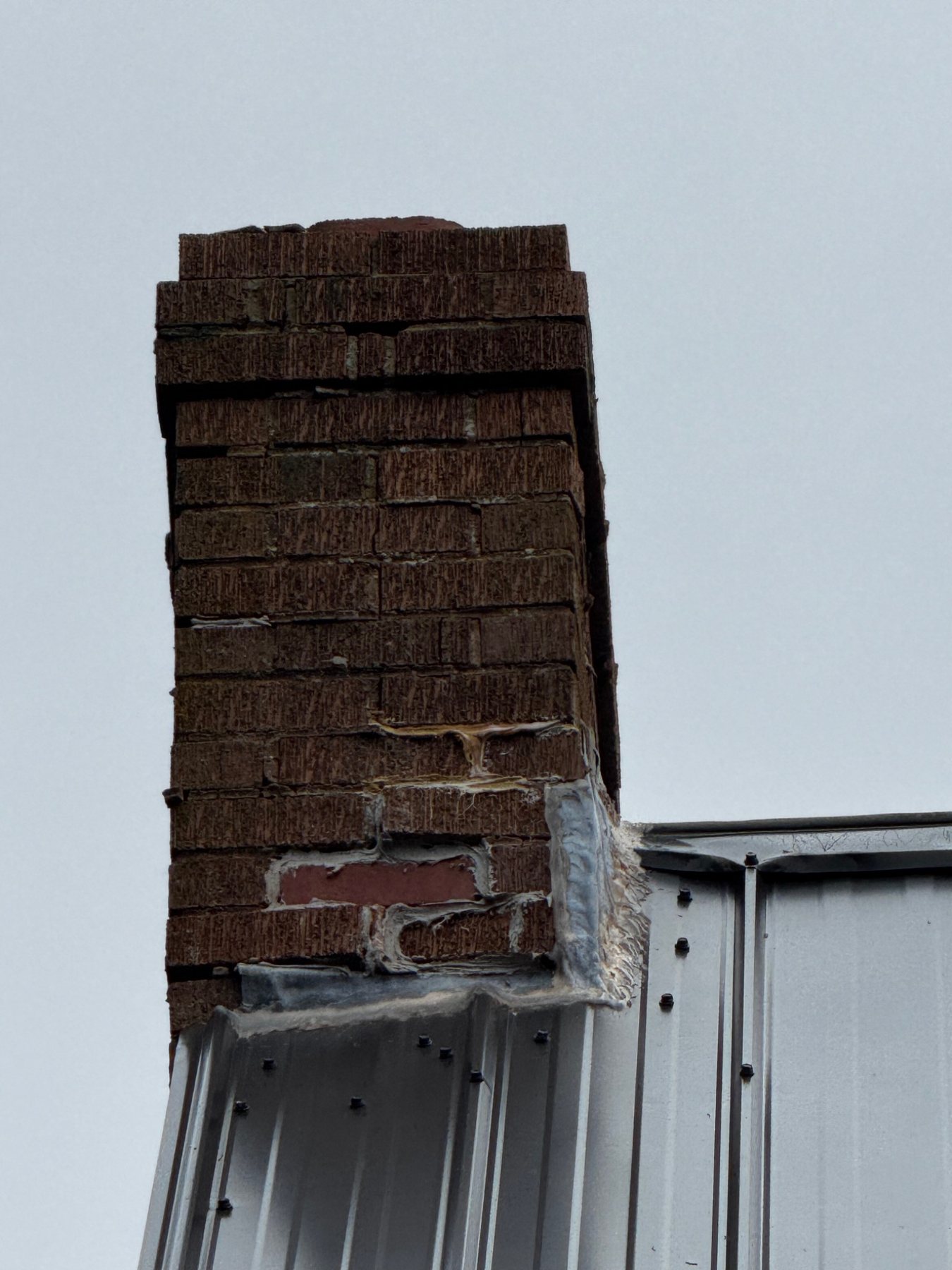 Aged chimney flashing and patching at a metal roof intersection in PEI
