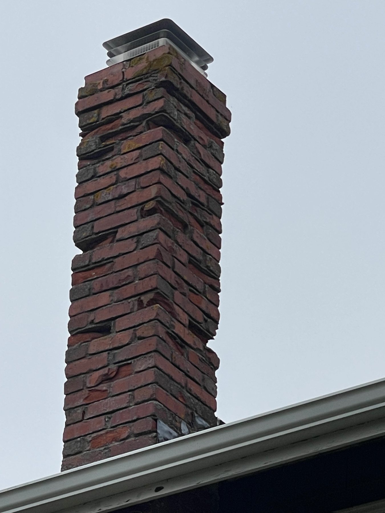 Severe mortar loss and displaced brick courses on a tall masonry chimney in PEI