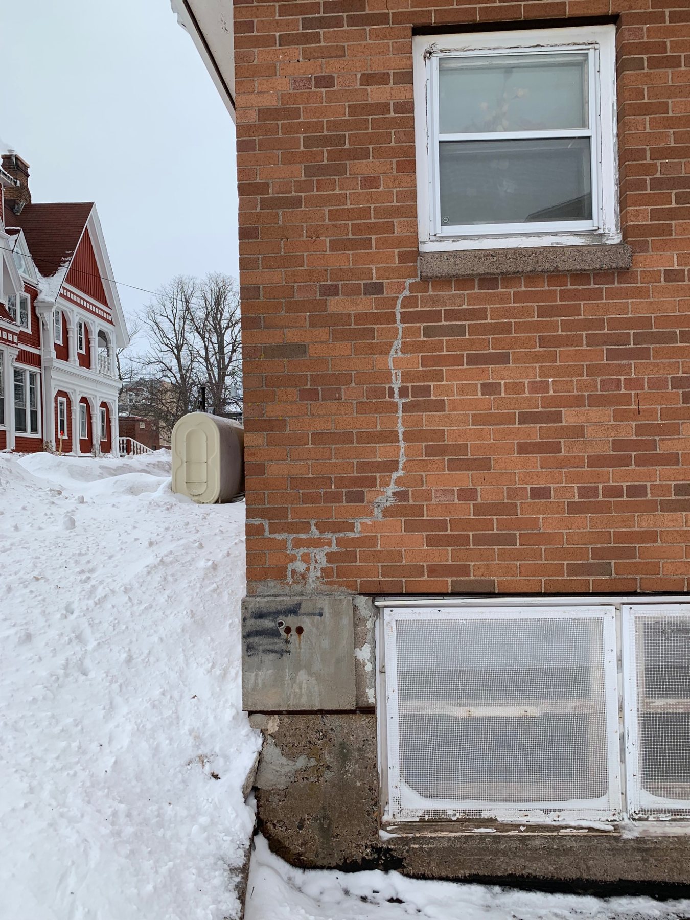 Vertical and stepped crack extending below a masonry window opening on a PEI brick building